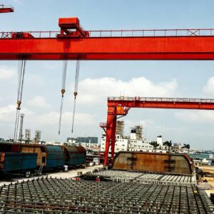 Shipbuilding gantry crane lifting large hull block over shipyard dry dock